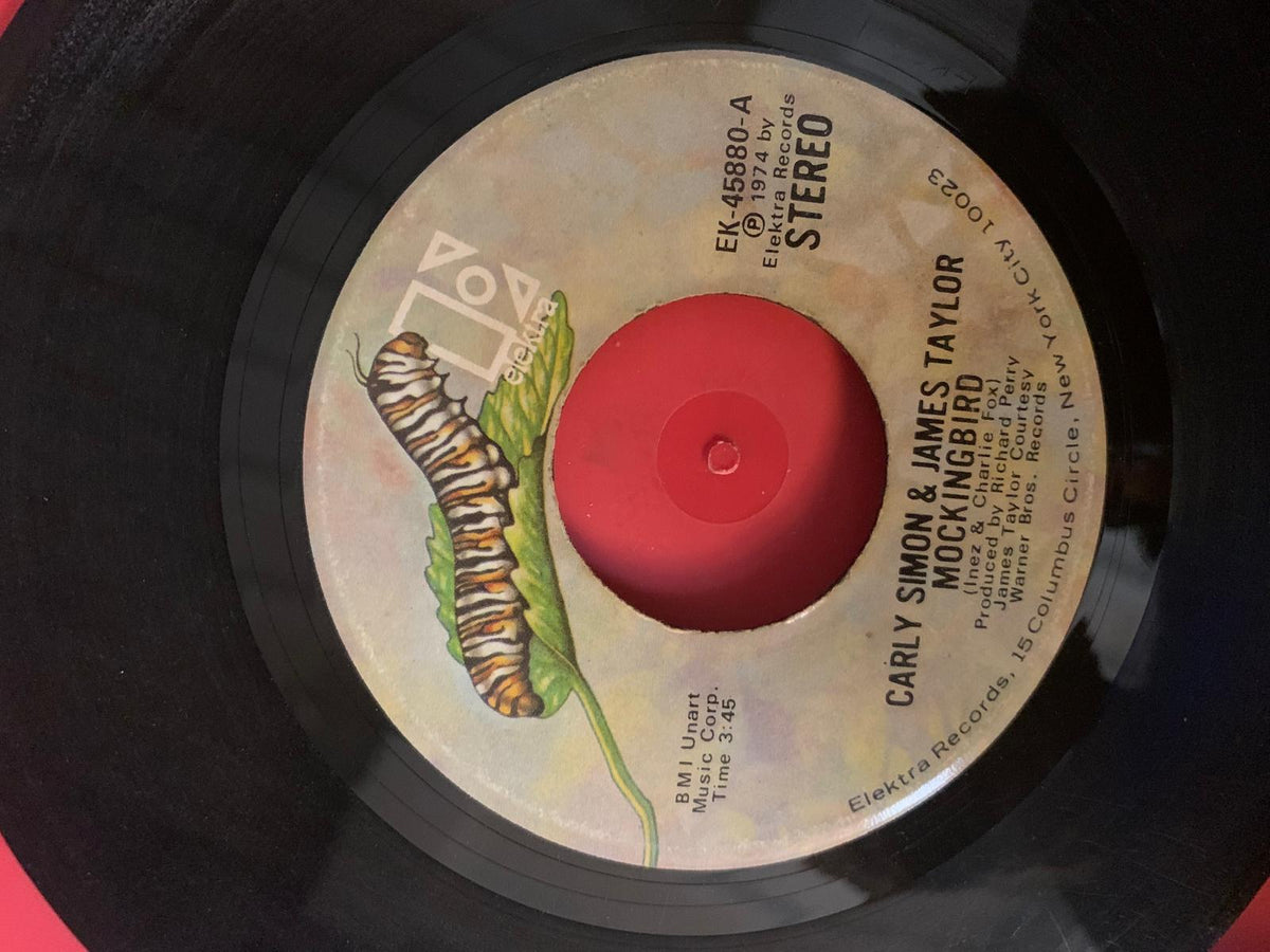 A vintage black vinyl record with a beige caterpillar label for mockingbird by carly simon and james taylor from elektra records