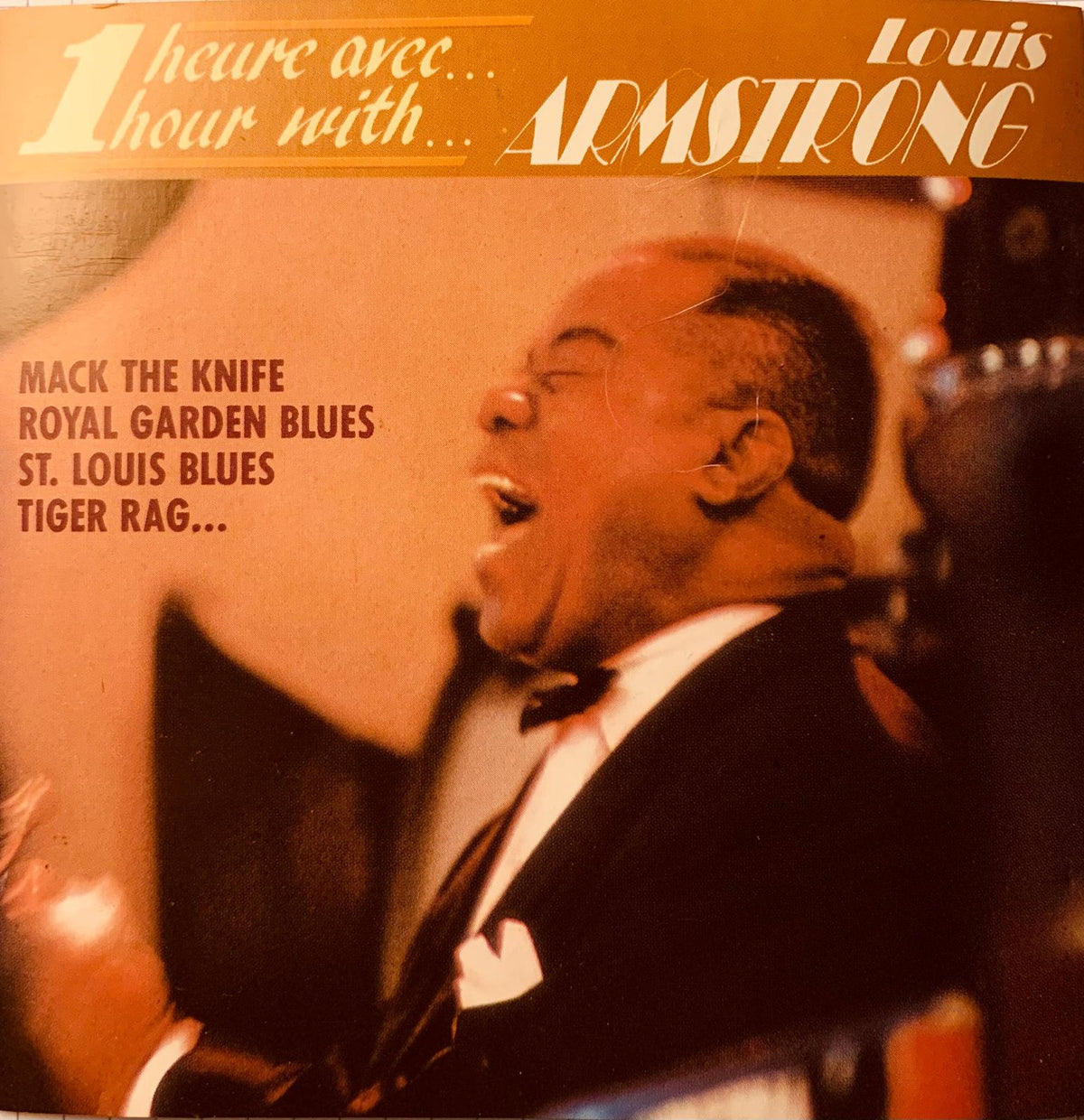 Vintage orange vinyl record album cover featuring Louis Armstrong in a black tuxedo titled 1 heure avec