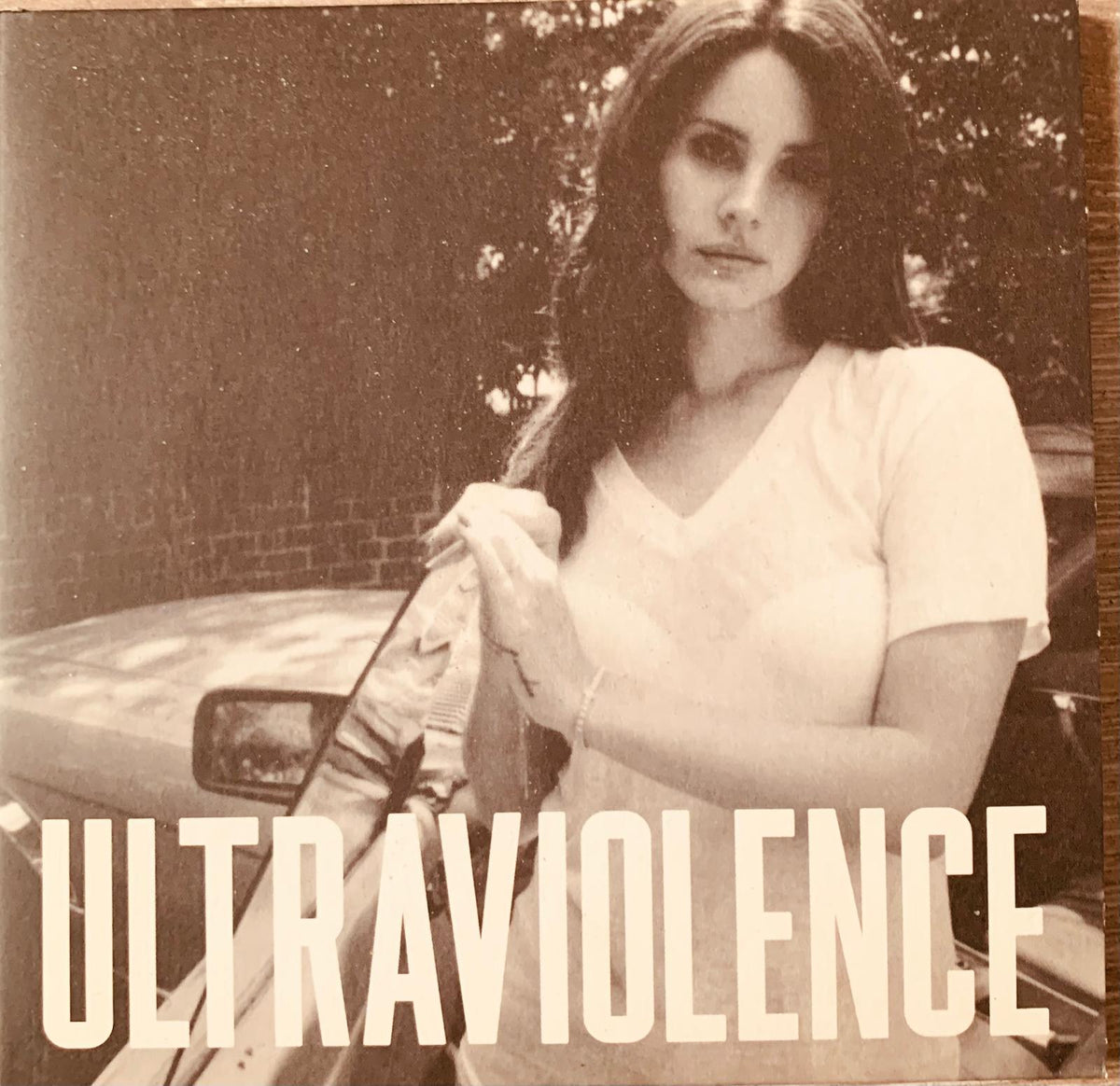Sepia-toned album cover of lana del rey ultraviolence original cd featuring woman in white v-neck t-shirt beside car