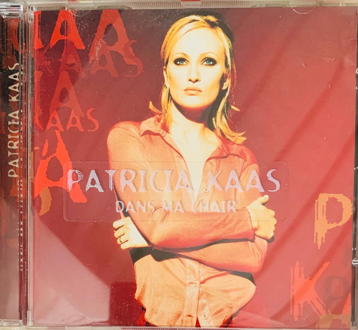 Red cd case of patricia kaas dans ma chair featuring her portrait in an orange shirt on a red background