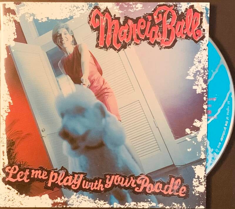 The album cover for marcia ball let me play with your poodle shows a woman in red standing behind a fluffy white dog