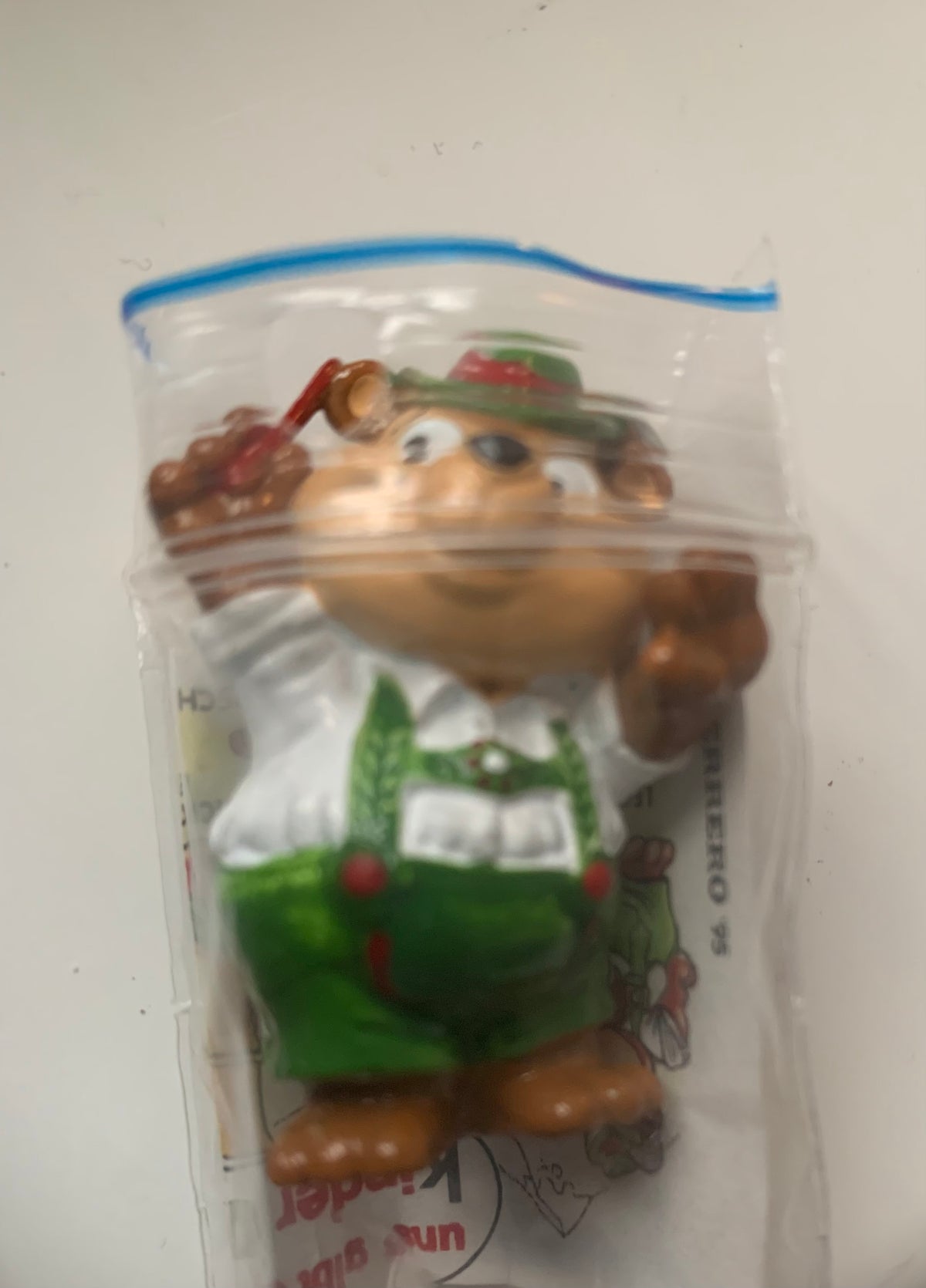 A brown plastic figurine from figurines dragon featuring a smiling character in green overalls and hat packaged in clear plastic