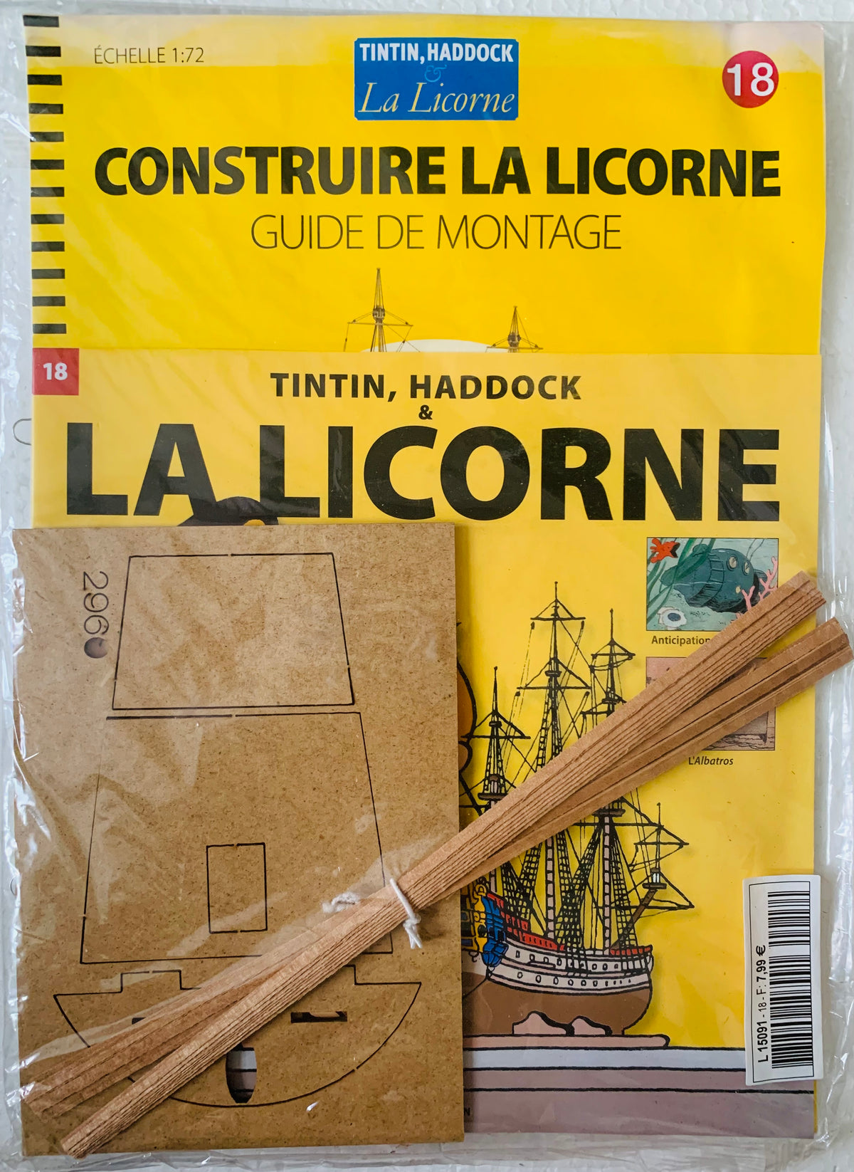 Yellow booklet titled La Licorne with black ship illustrations alongside brown cardboard cutouts and wooden model sticks