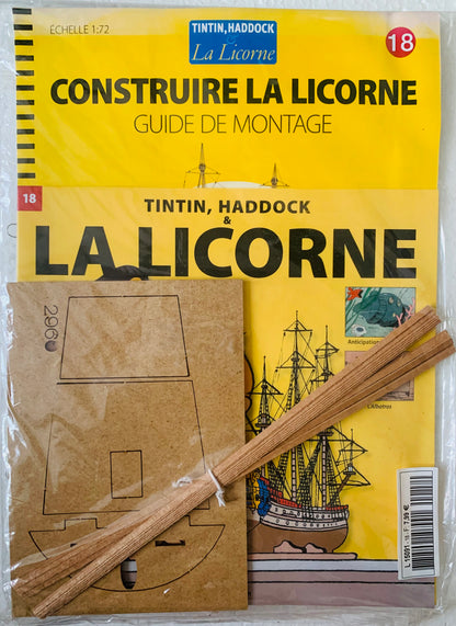 Yellow booklet titled La Licorne with black ship illustrations alongside brown cardboard cutouts and wooden model sticks