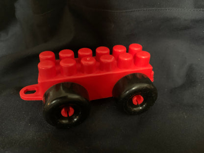 Red plastic toy wagon with black wheels and red axles featuring a classic brick-style design in toys 001