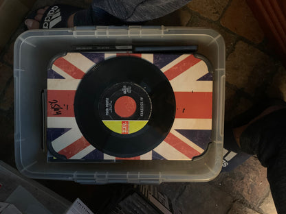 Black vinyl record with red center label and yellow ring featuring peggy lee classics iv on union jack surface in plastic bin