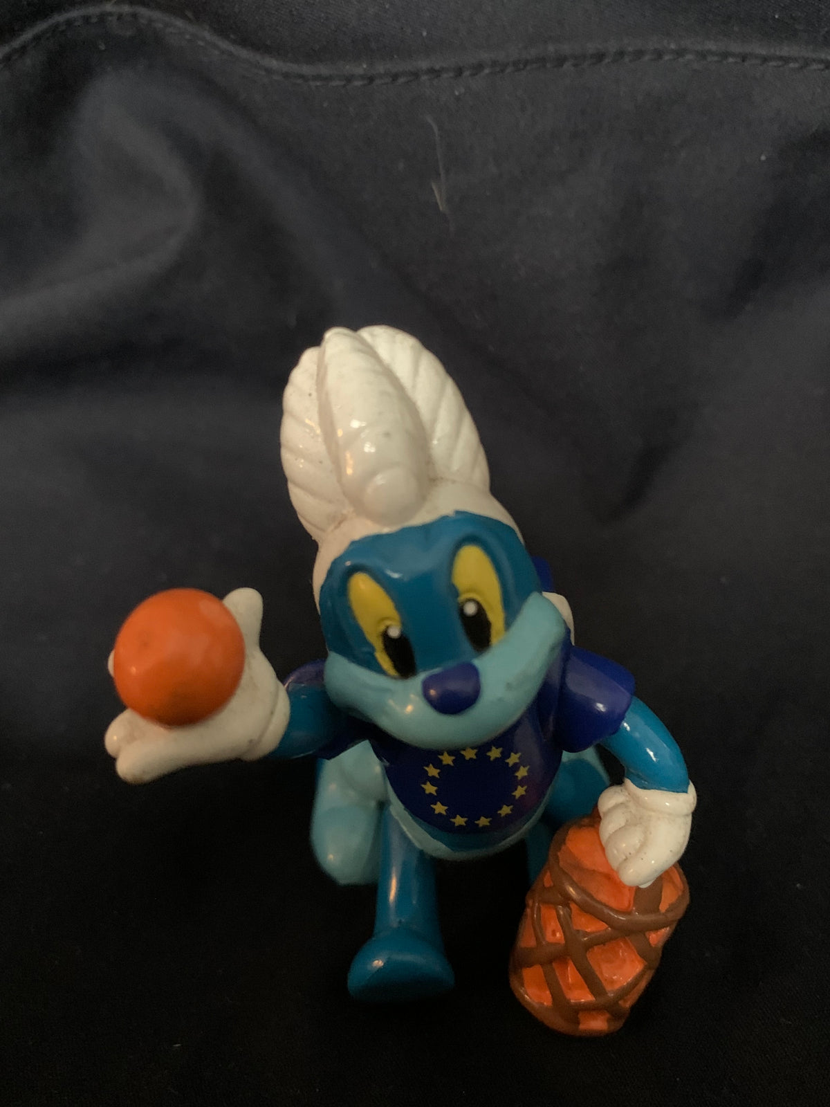 Blue and white plastic cartoon figurine with yellow eyes holding an orange basketball wearing a eu flag vest toys 001