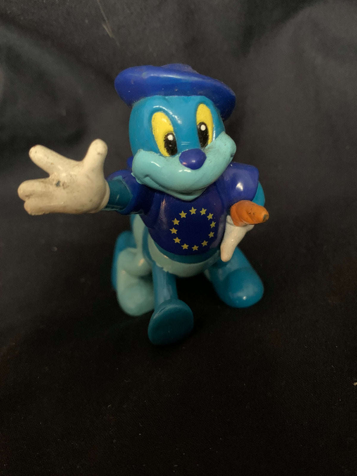 Blue plastic figurine toy wearing blue hat and vest with yellow stars holding orange carrot from toys 001 collection