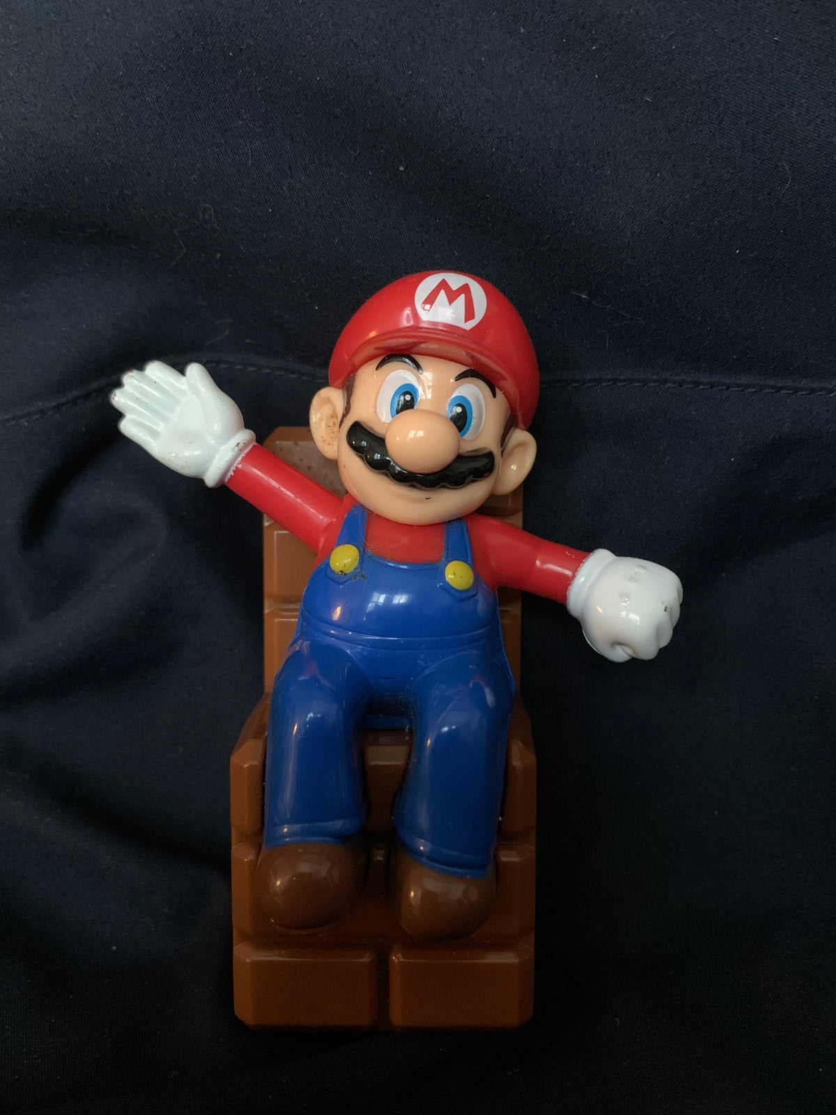 Red and blue plastic mario figurine with white gloves seated on a brown block base in toys 001 collection