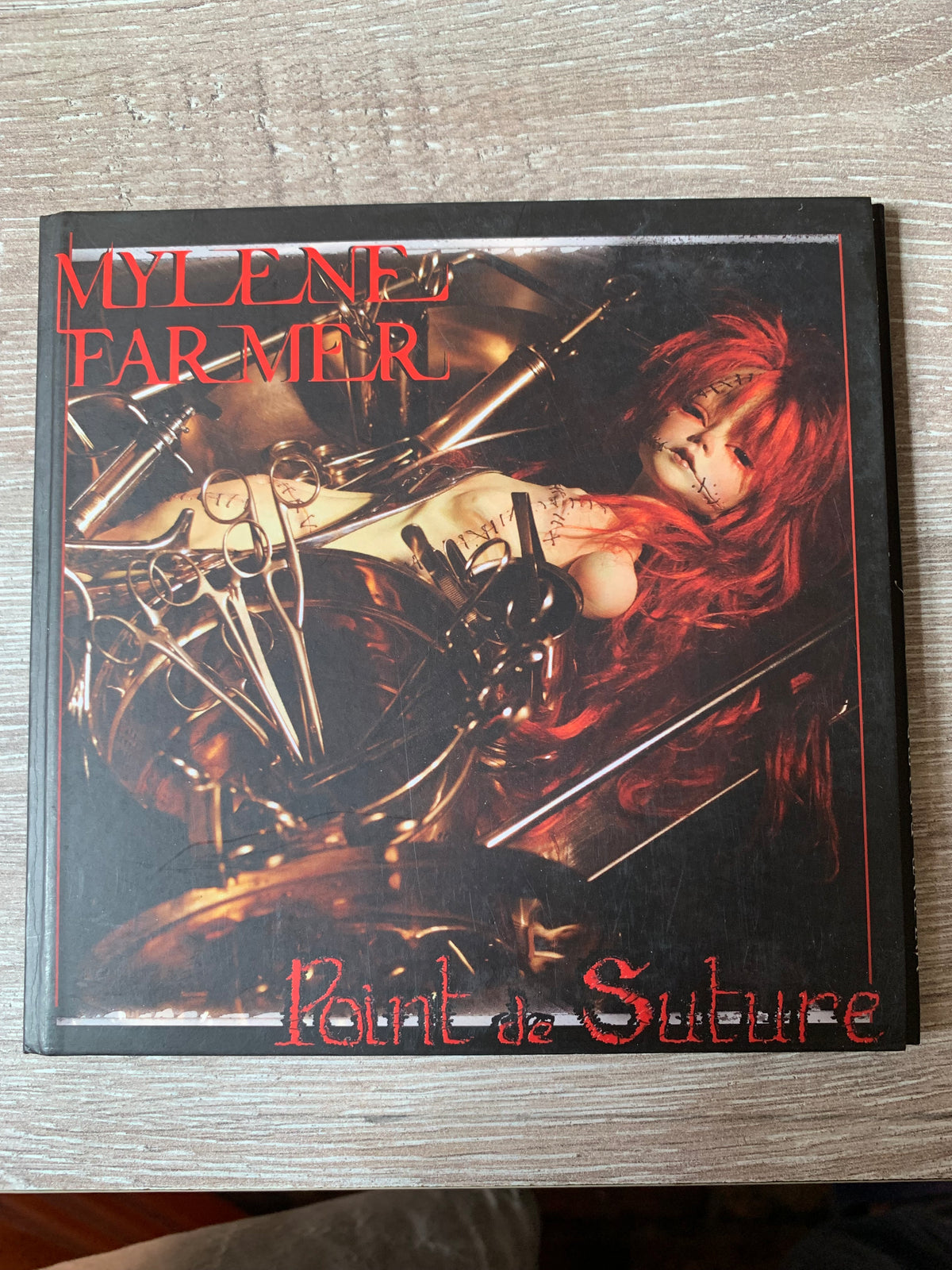 Cd 001 featuring Mylene Farmer point de suture album cover with red-haired stitched doll and surgical instruments on dark background
