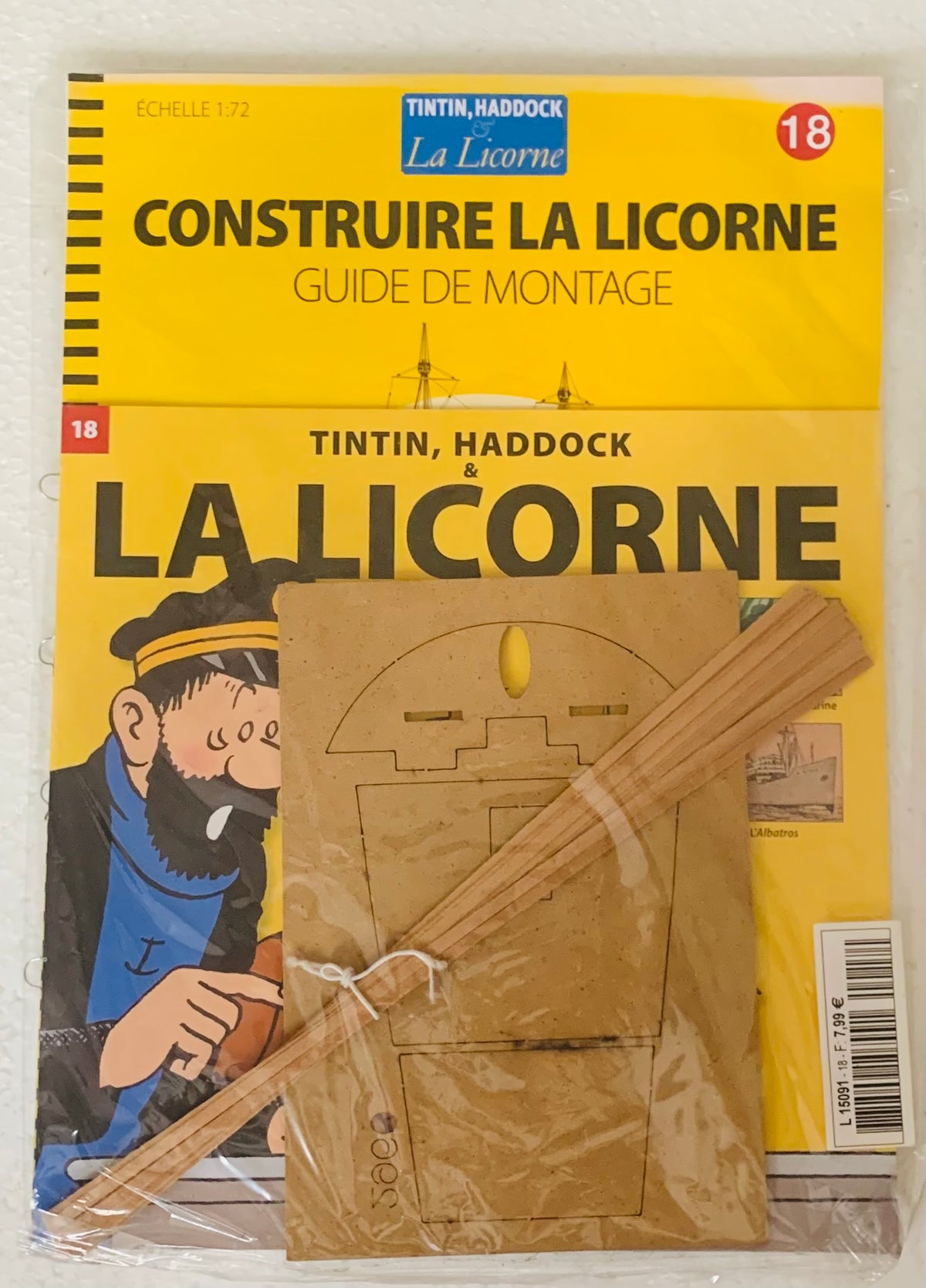 Yellow booklet titled construire la licorne with tintin and haddock illustration and wooden craft pieces for building the ship