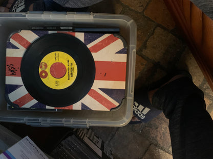 Black vinyl soul 7 inch record with yellow label featuring red and white text on union jack surface inside plastic bin
