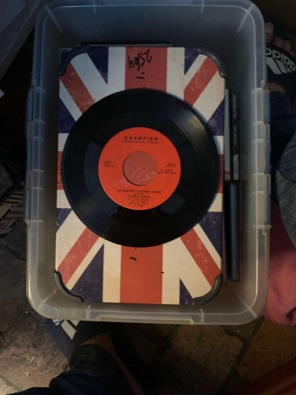 Black vinyl soul 7 record with orange center label by champion on union jack surface inside clear storage bin