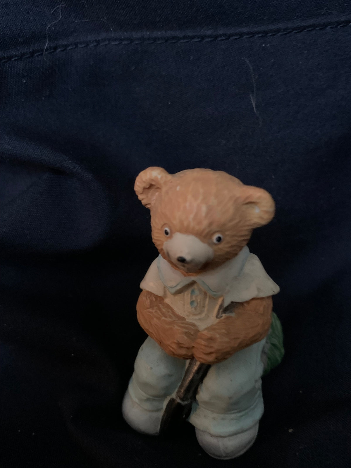 A small tan ceramic teddy bear figurine dressed in light blue holding a miniature shovel from toys 001