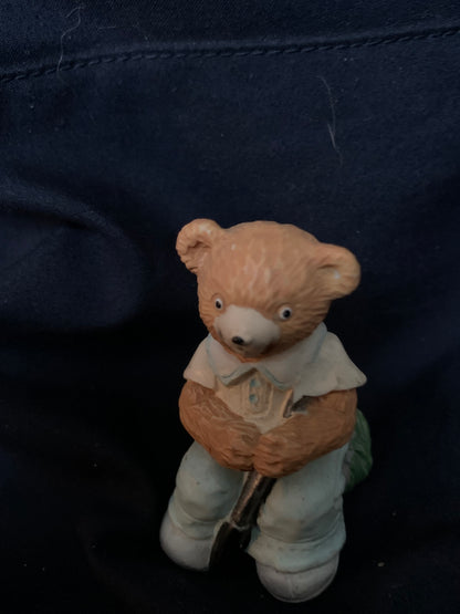 A small tan ceramic teddy bear figurine dressed in light blue holding a miniature shovel from toys 001