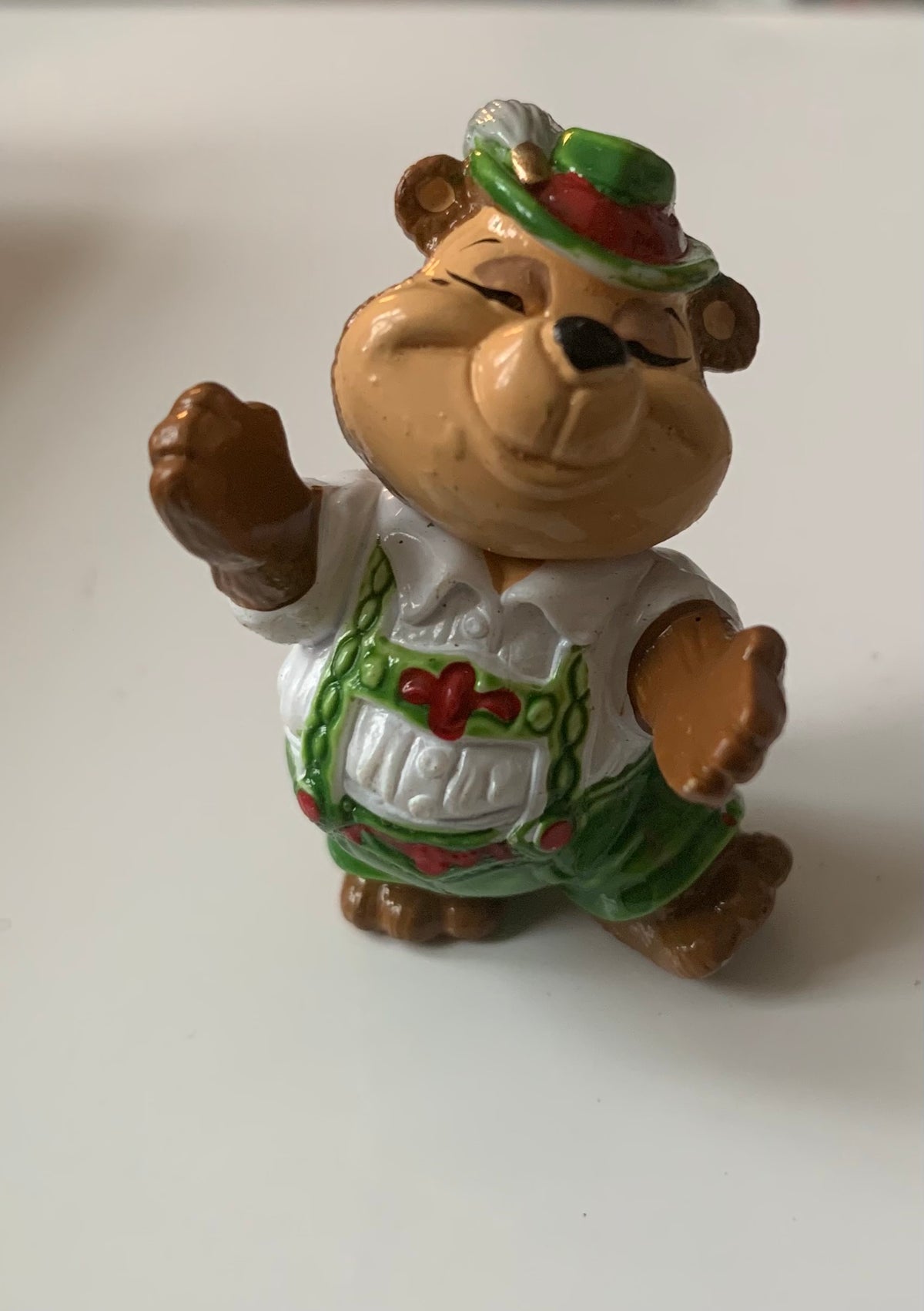 A cheerful brown bear figurine in a green white traditional outfit with red accents and matching green hat from figurines dragon