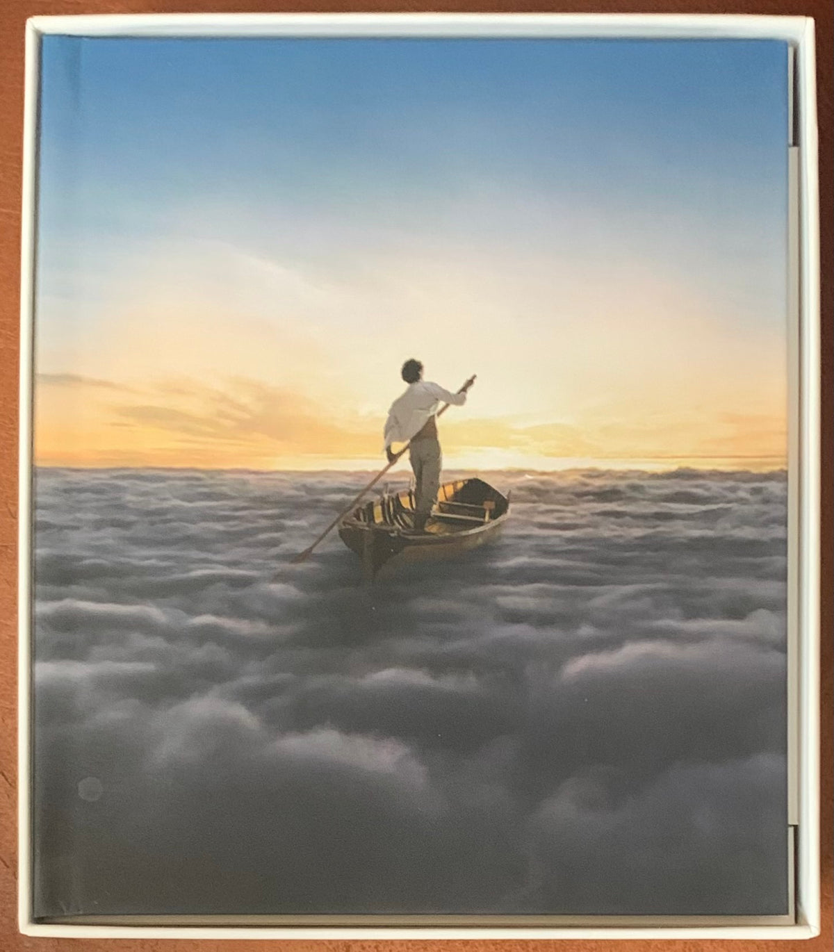 A serene illustration on a wooden rowboat with a man paddling through clouds at sunset in endless river