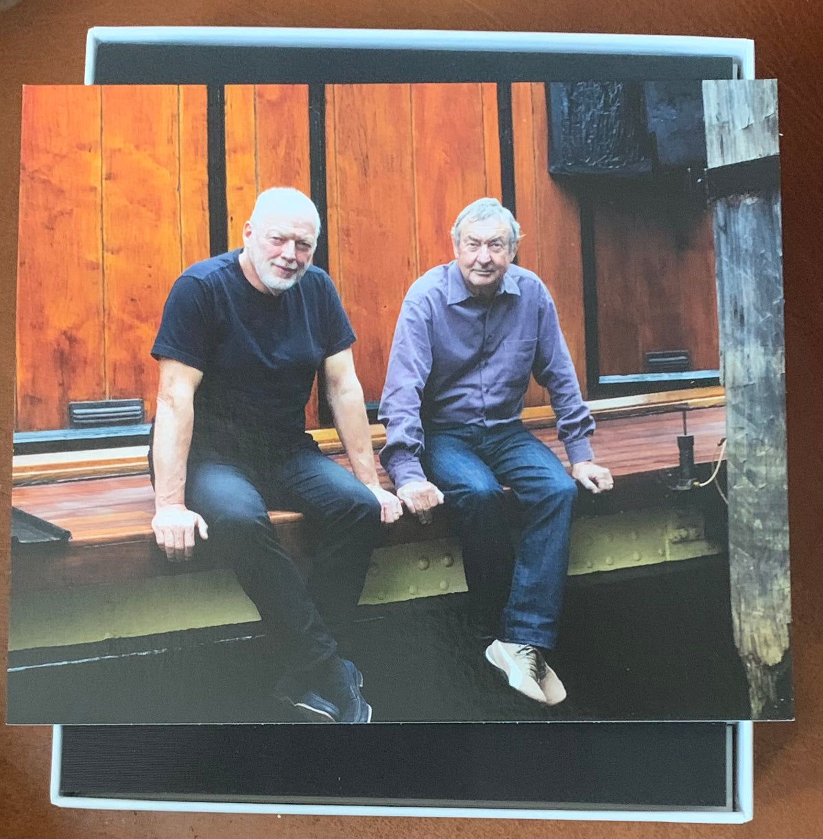 A framed photograph titled endless river showing two men seated on a wooden bench wearing black and purple clothing