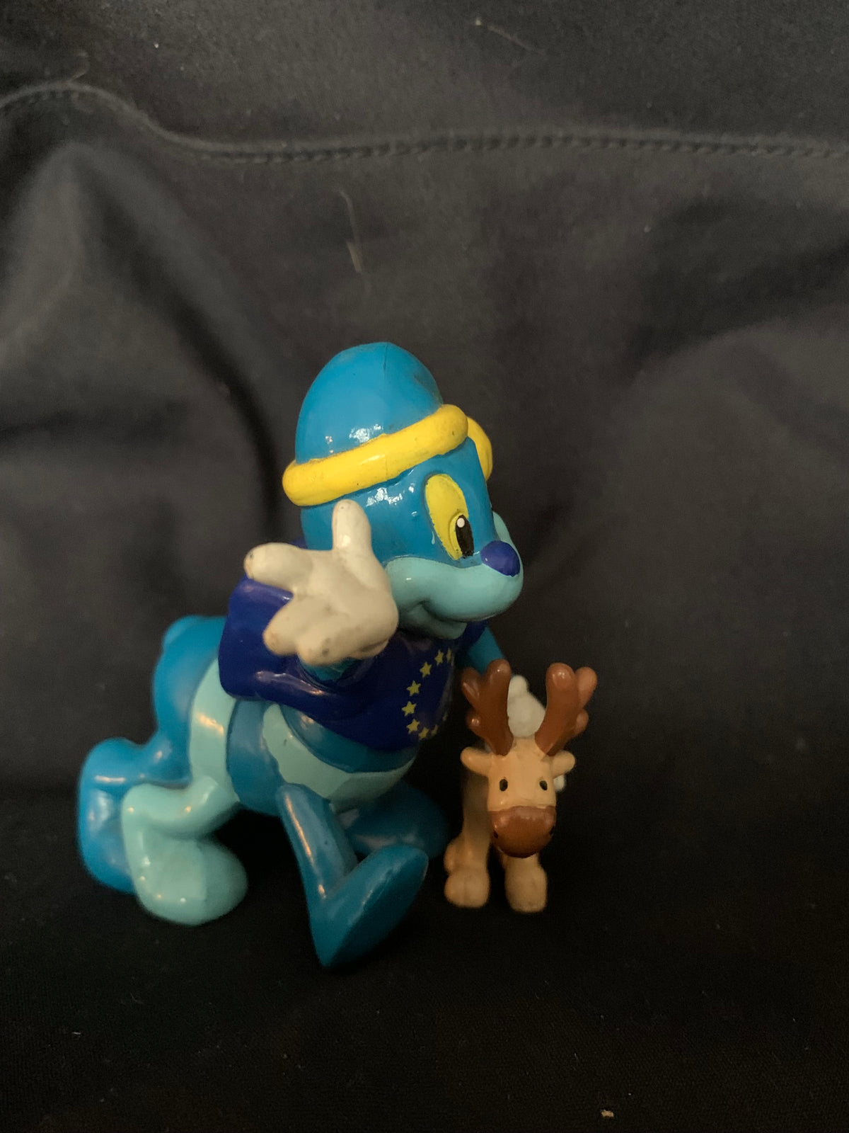 Blue and teal plastic cartoon figurine with yellow-trimmed hat standing beside a smaller brown reindeer toy 001