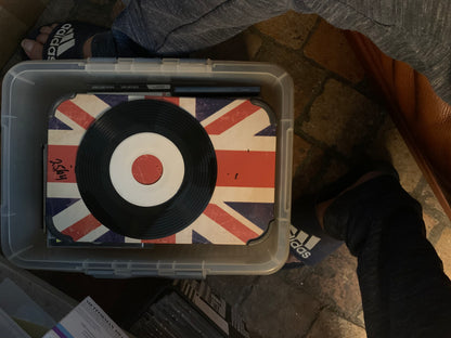 Black vinyl record soul 7 with white center and red dot resting on union jack surface inside clear plastic bin