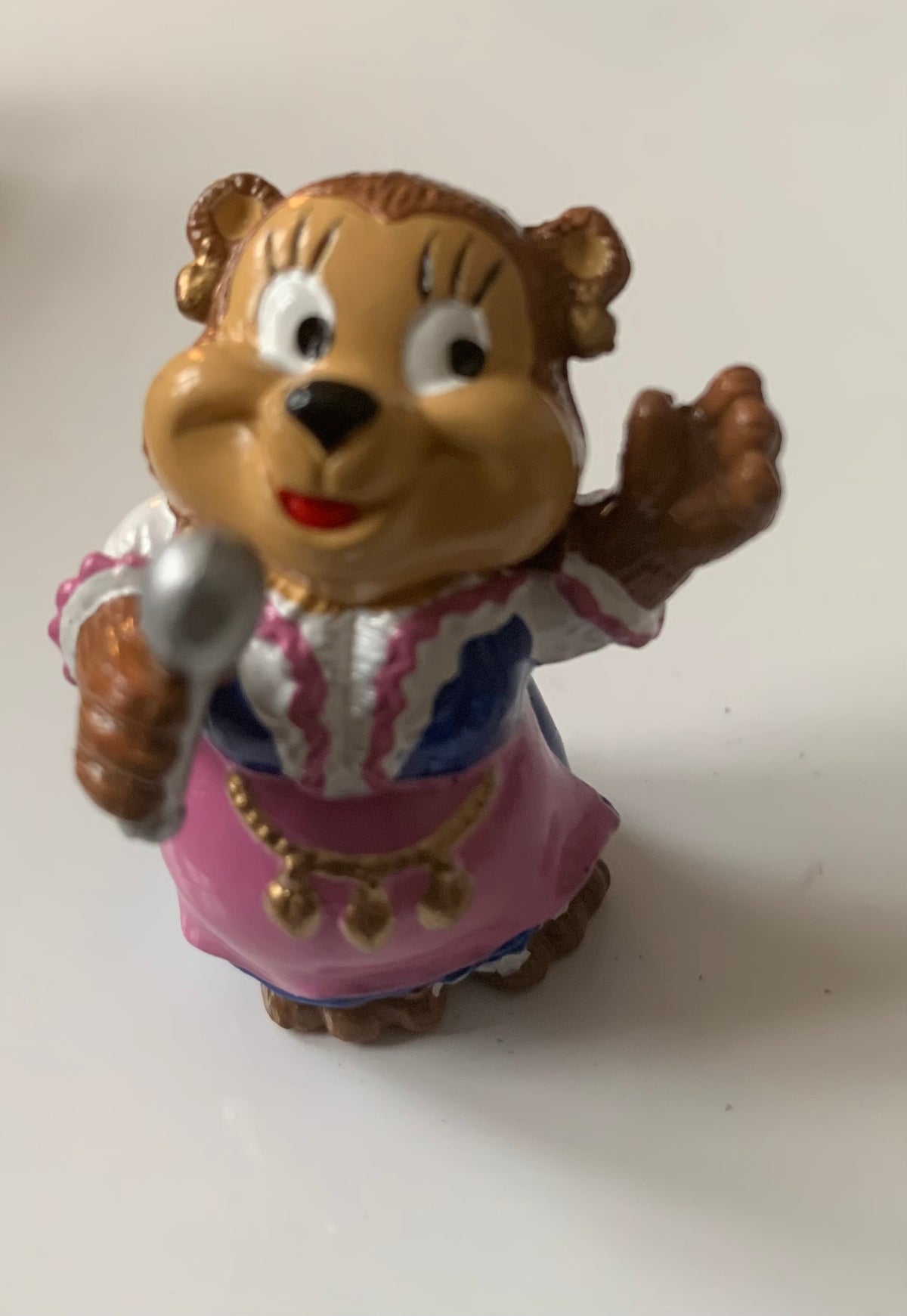 A cheerful brown bear figurine dressed in a pink and white striped dress with blue accents holding a silver spoon from figurines dragon