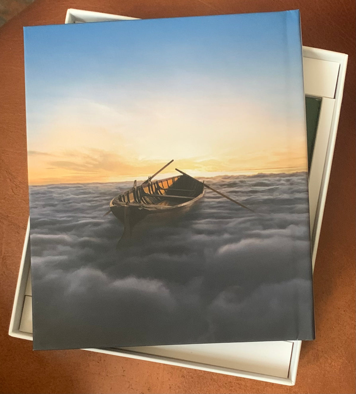 Hardcover book endless river with a vivid cover showing a weathered wooden rowboat floating on clouds at sunset