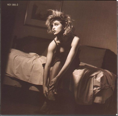 A woman with light-colored hair sits on a bed wearing a dark sleeveless top and sheer stockings on Madonna Like A Virgin cd album cover