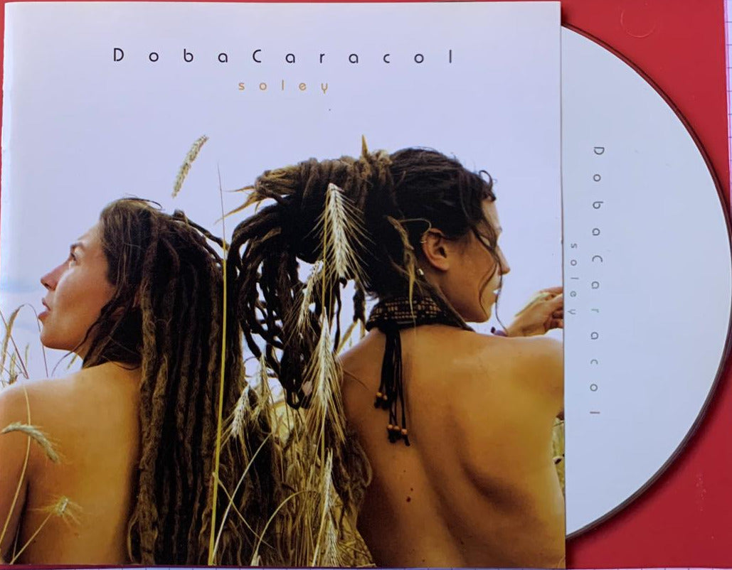 The album cover for Soleil by Doba Caracol shows two women with long dark dreadlocks adorned with wheat strands and beads