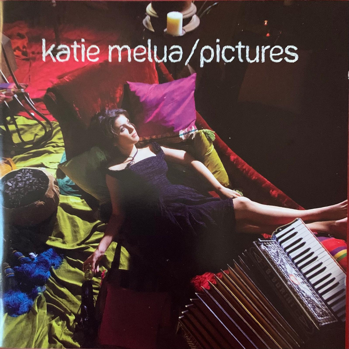 A woman in a black dress reclines on colorful fabrics next to an ornate accordion on Katie Melua Pictures CD cover