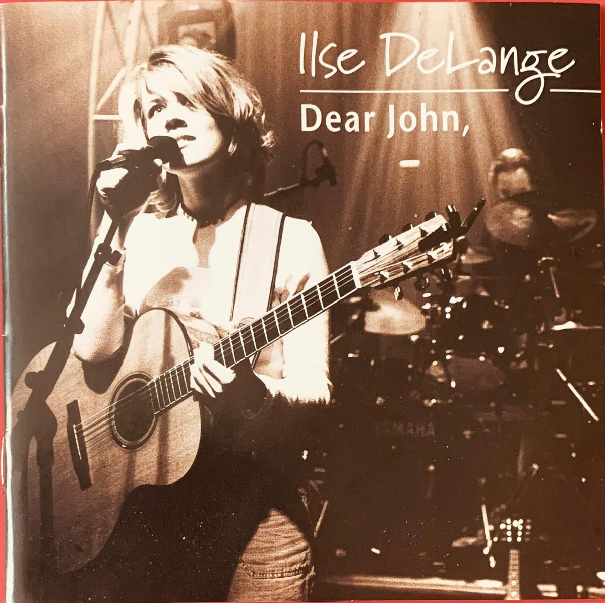A sepia-toned acoustic guitar with natural wood finish and dark fretboard held by performer on stage for ilse delange dear john cd