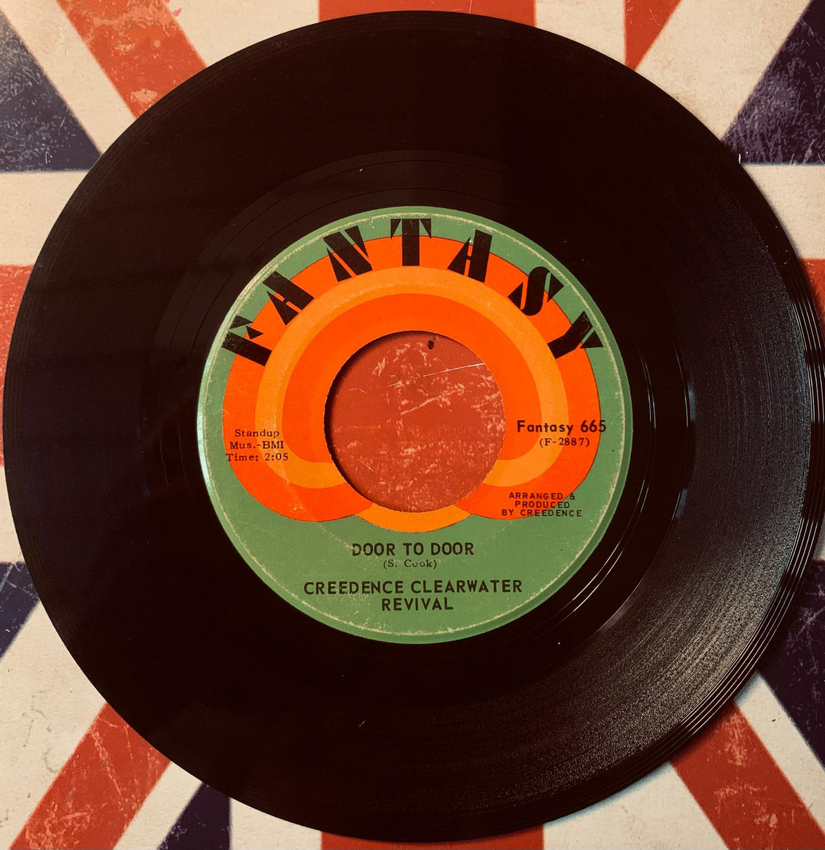 A vintage black vinyl record featuring a colorful orange and green fantasy label with song door to door by Creedence Clearwater Revival