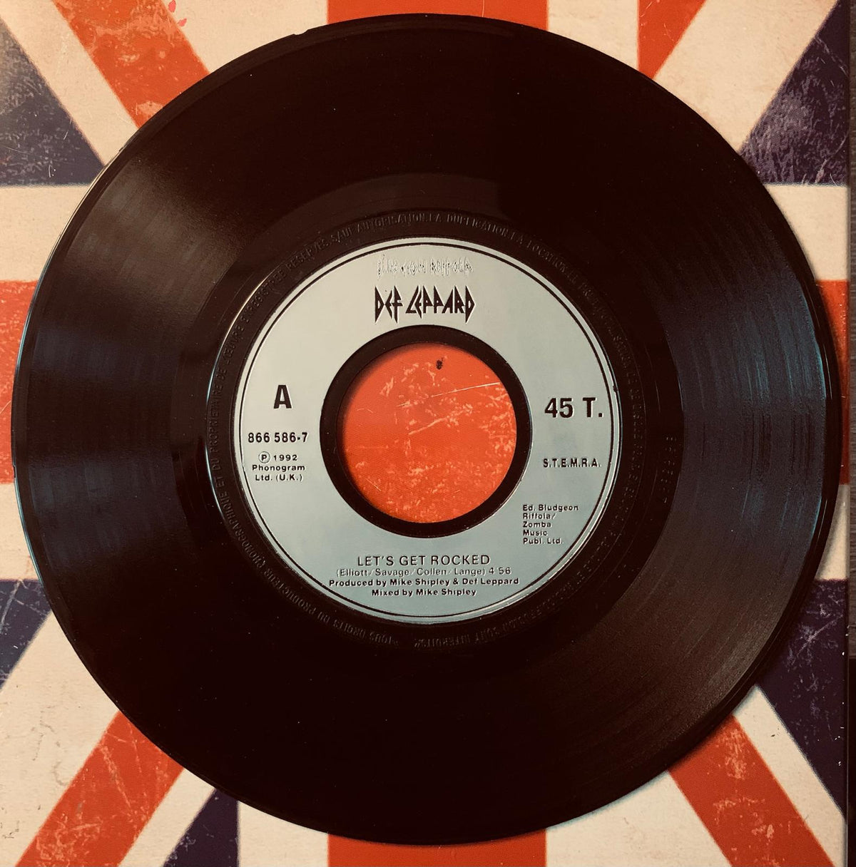 Black vinyl 45 rpm record with white label and orange center playing lets get rocked by def leppard original 45t vinyl