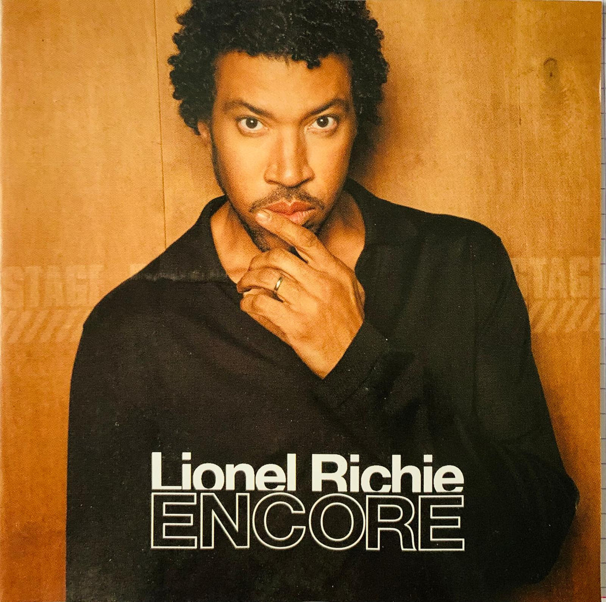 Lionel richie wearing a black long-sleeved shirt with hand on chin on the encore original cd cover usa edition