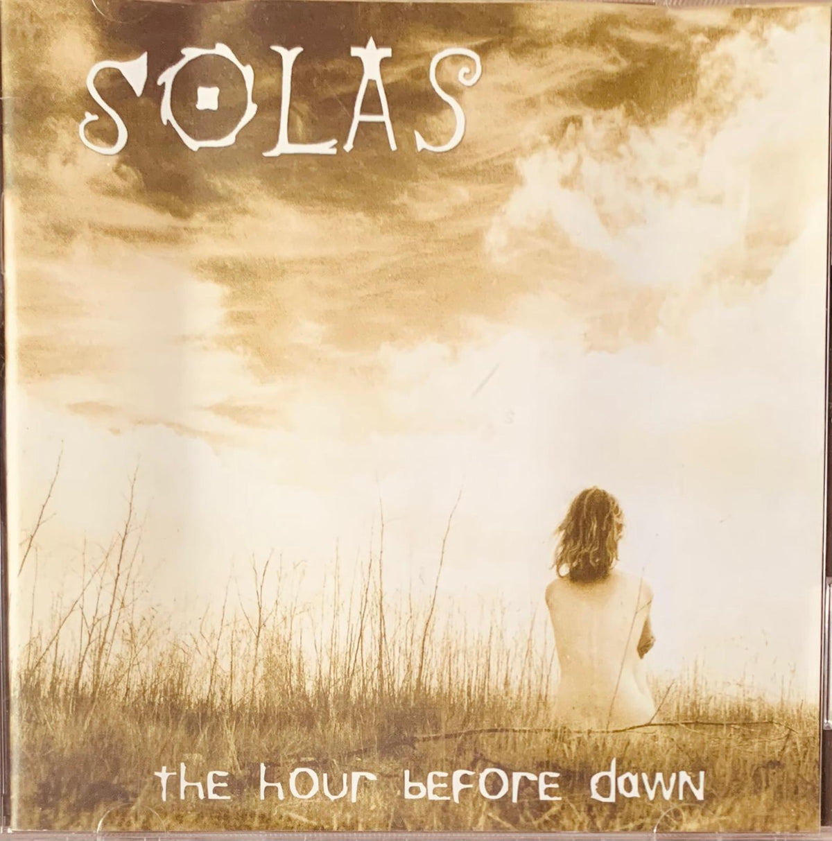 Sepia toned cd album cover of solas the hour before dawn showing a solitary figure seated in tall grass under sky