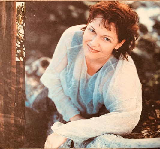 A woman with short wavy brown hair wearing a light blue sheer blouse over a white top on a classical vocal CD cover