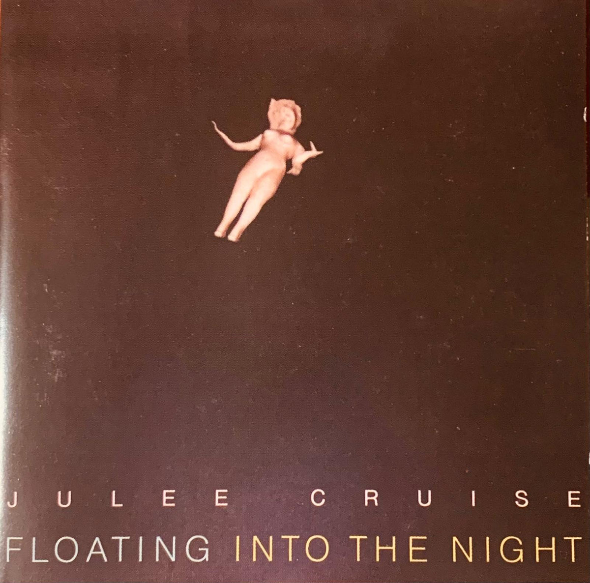 A dark brown CD album cover of julee cruise floating into the night featuring a small nude figurine