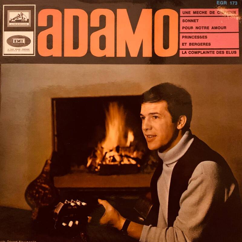 Adamo album cover featuring a warm-toned photo of the artist in a dark vest over white turtleneck by a fireplace