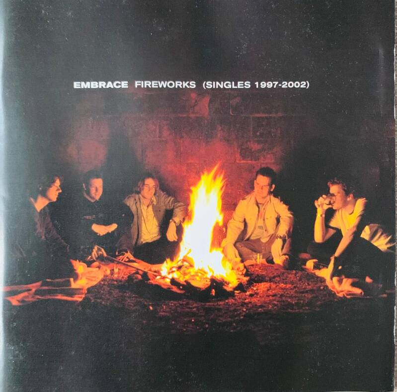 The album cover for Embrace Fireworks singles 1997-2002 shows six people around a glowing campfire at night